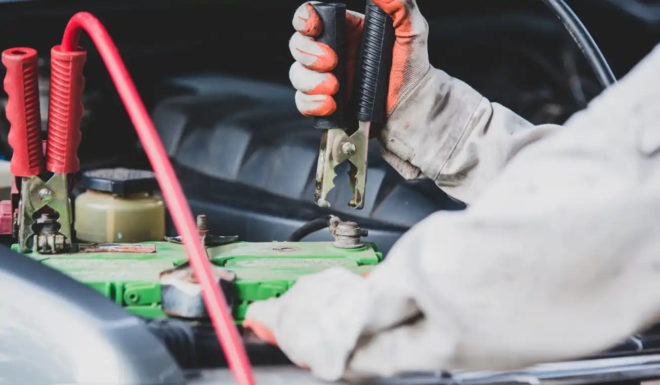 Gloved hand holding jumper cables connected to a car battery during a jump-start process.