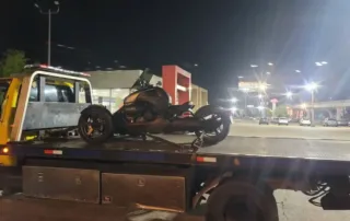 flatbed tow truck transporting a motorcycle at night in a brightly lit urban area.