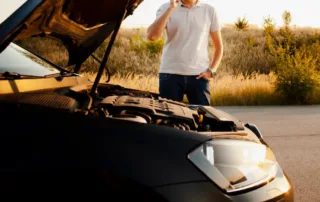 standing near a car with its hood open, signaling a vehicle breakdown on a rural road.