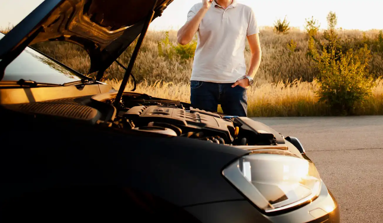 standing near a car with its hood open, signaling a vehicle breakdown on a rural road.