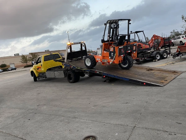 A yellow flatbed tow truck efficiently loads an orange forklift in a parking lot, demonstrating reliable towing services for industrial equipment.