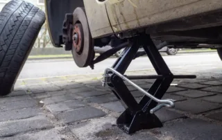 Car lifted on a jack with a removed wheel and a spare tire ready for replacement on a brick-paved surface