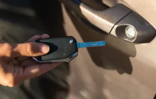 Hand holding a car key near the door handle, preparing to unlock the vehicle.