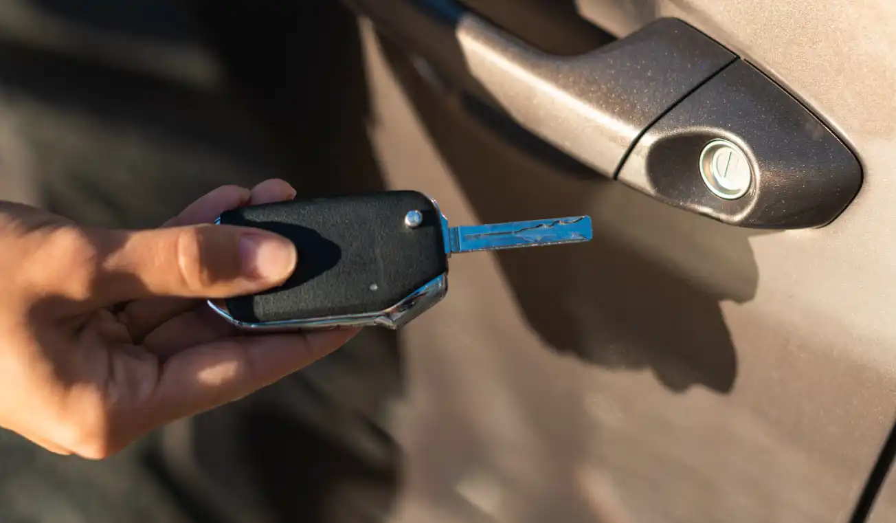 Hand holding a car key near the door handle, preparing to unlock the vehicle.