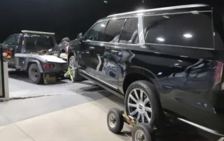 Black SUV being towed by a tow truck with a wheel lift and dollies at night in a well-lit gas station Medium Duty Towing