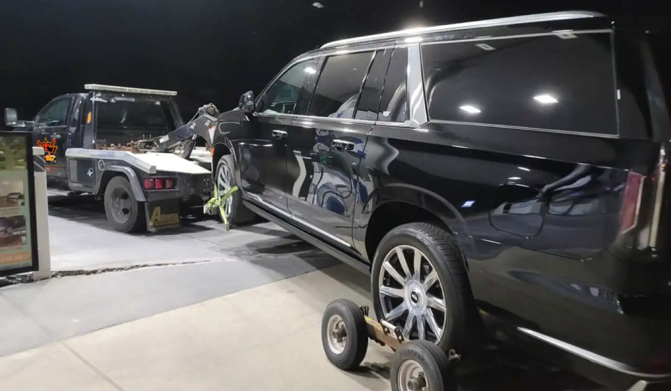 Black SUV being towed by a tow truck with a wheel lift and dollies at night in a well-lit gas station Medium Duty Towing