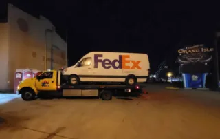 flatbed tow truck safely transports a FedEx delivery van at night, showcasing reliable towing solutions for commercial vehicles.