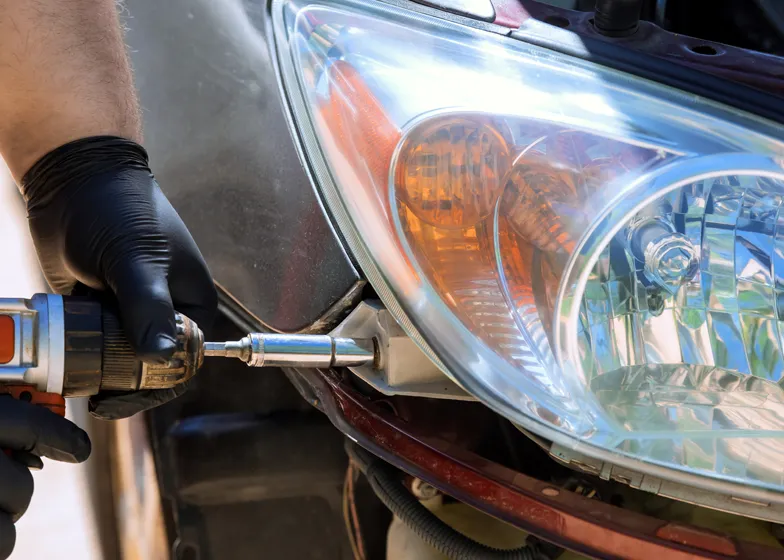 Technician using a power tool to repair and secure a car headlight, providing professional lighting and electrical power assistance for vehicle safety and visibility