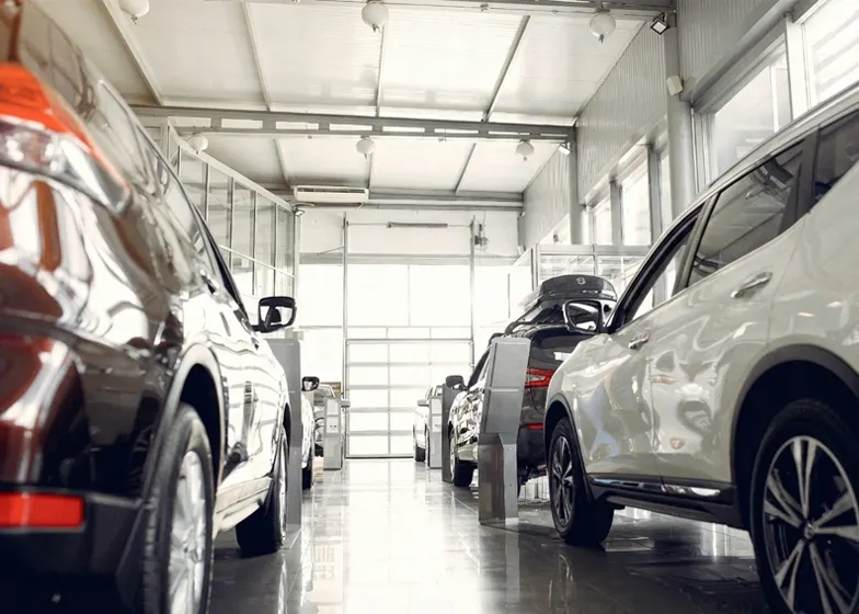 Inside a modern vehicle storage facility, showcasing several luxury cars lined up in a well lit showroom with large windows and polished floors.