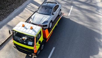 Luxury and exotic car towing service with a silver luxury car being loaded onto a flatbed tow truck on a clear road.