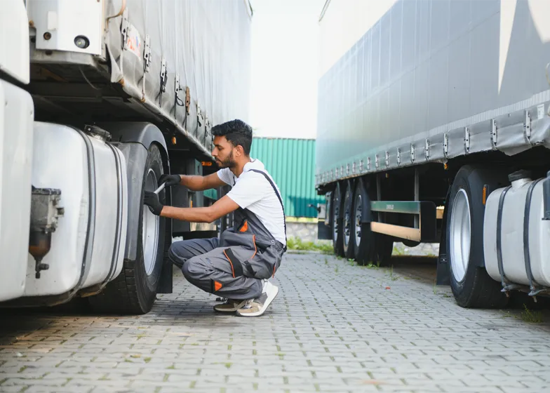 Worker performing tire inspection on a large cargo truck, providing essential maintenance and cargo recovery support.