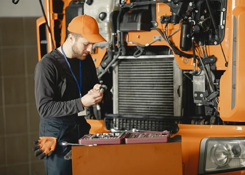 Mechanic in an orange cap working on the engine of a heavy-duty truck, providing commercial recovery support and maintenance services.