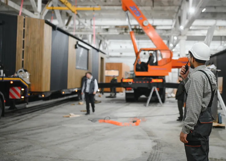 Exhibition unit towing service with a worker coordinating the unloading of a modular exhibition unit using a crane in a warehouse.