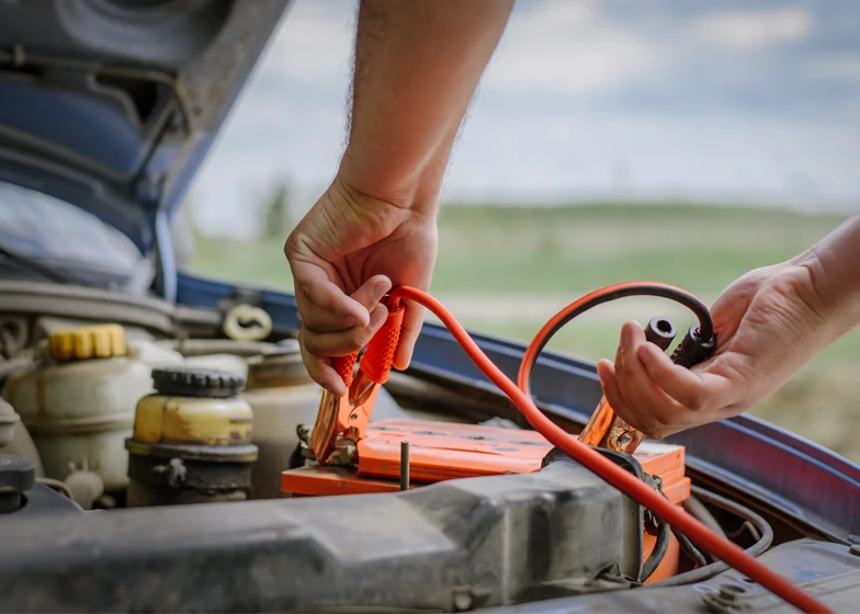 Battery jump start service with a person connecting jumper cables to a car battery for a quick power boost.