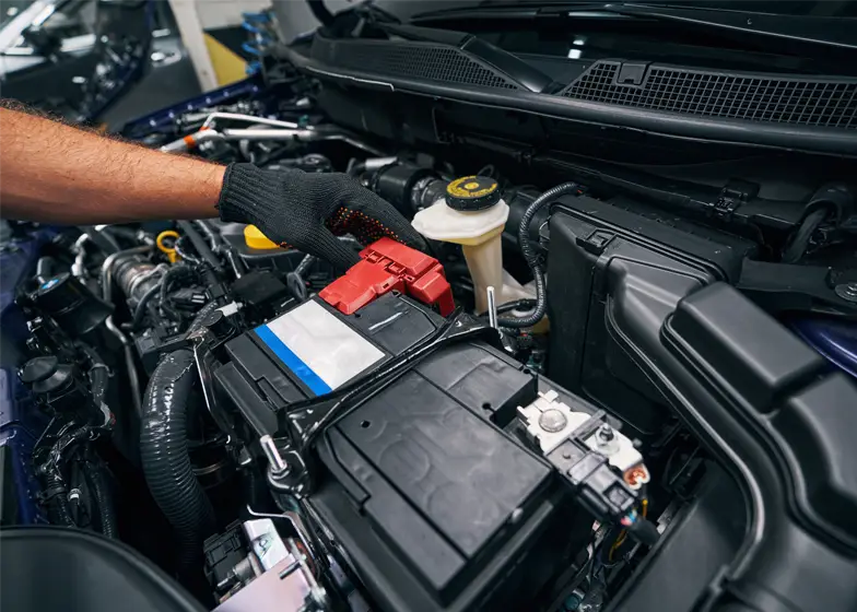 Breakdown recovery service with a mechanic checking and replacing the car battery under the hood for quick roadside assistance.