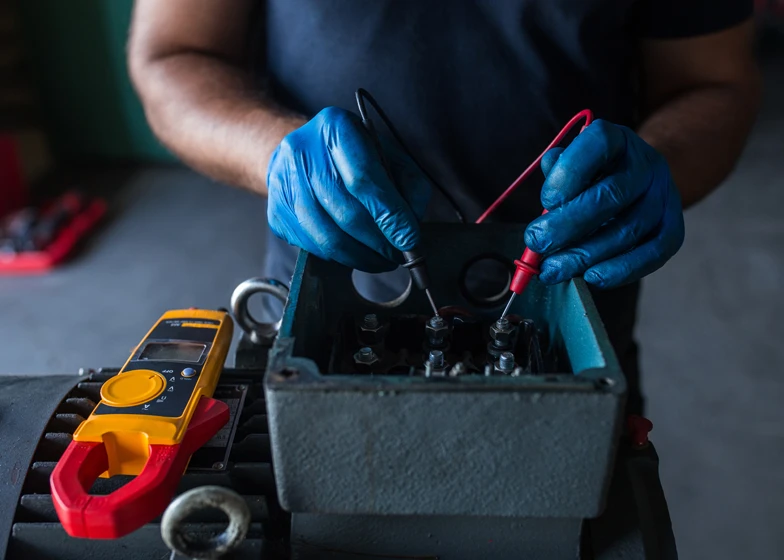 Mobile battery replacement service with a technician using a multimeter to check a vehicle battery in a garage.
