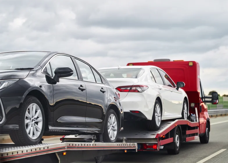 Private property towing service with two cars loaded on a flatbed tow truck on the road.