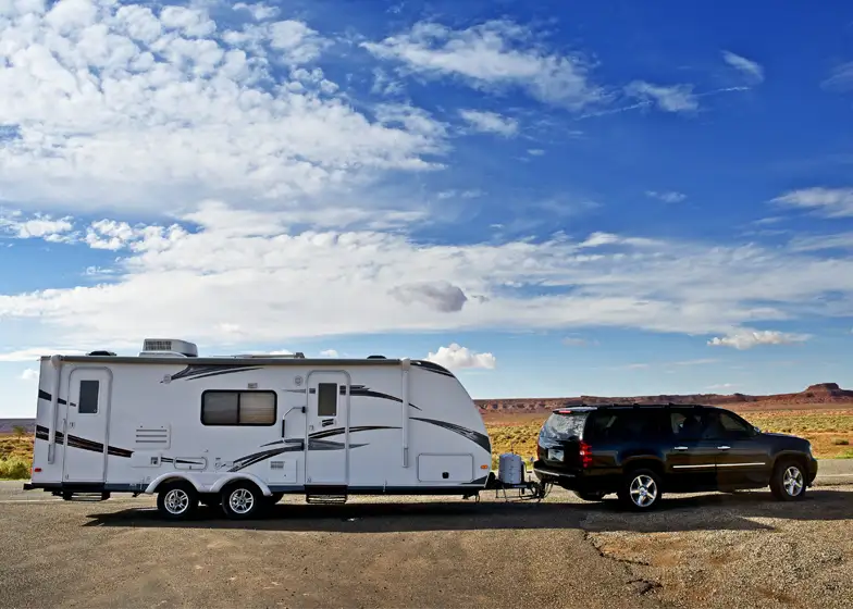 RV camper transport service with an SUV towing a large travel trailer on a scenic highway.