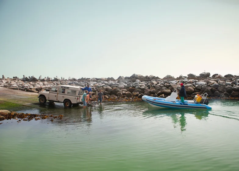 Boat and watercraft transport service with a vehicle launching a boat into the water while a motorized boat is being prepared nearby.