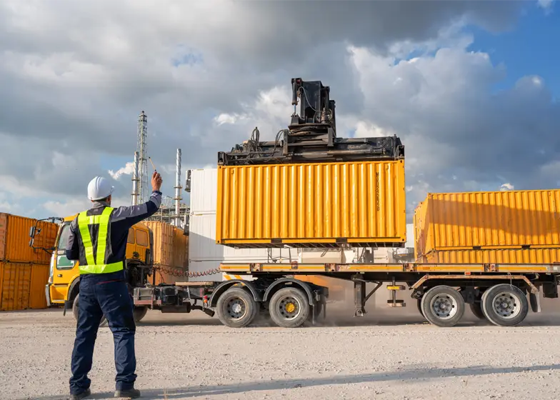 Heavy load transport service with a worker guiding a large shipping container being loaded onto a trailer by a crane.
