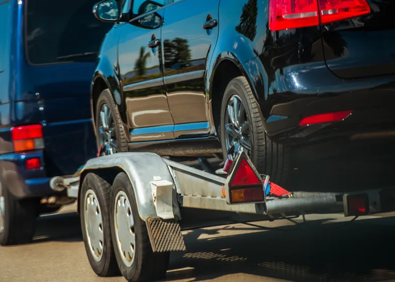 Local towing service with a black car being towed on a flatbed trailer on a sunny day.