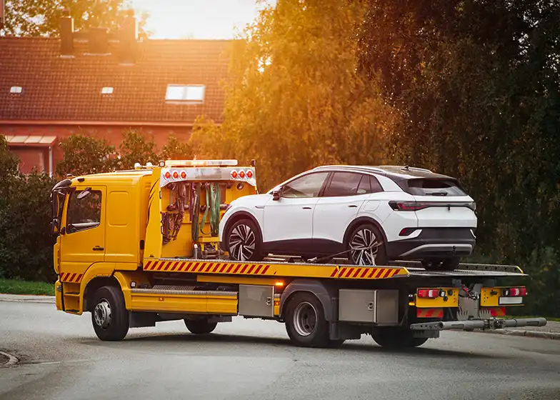 Long-distance towing service with a yellow tow truck carrying a white vehicle on a flatbed for transport.