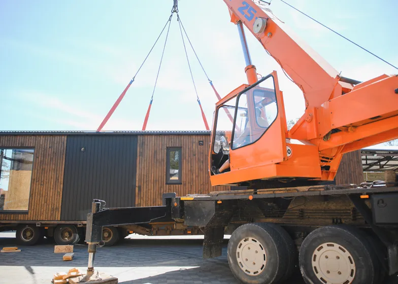 Portable housing towing service with a crane lifting a wooden mobile home onto a flatbed truck for transport.