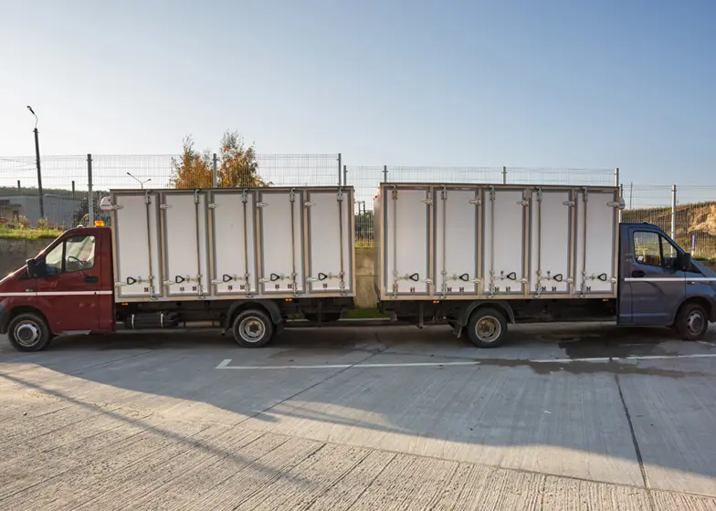 Two large trucks with enclosed cargo trailers parked side by side, ready for transporting goods with a professional trailer transport service.