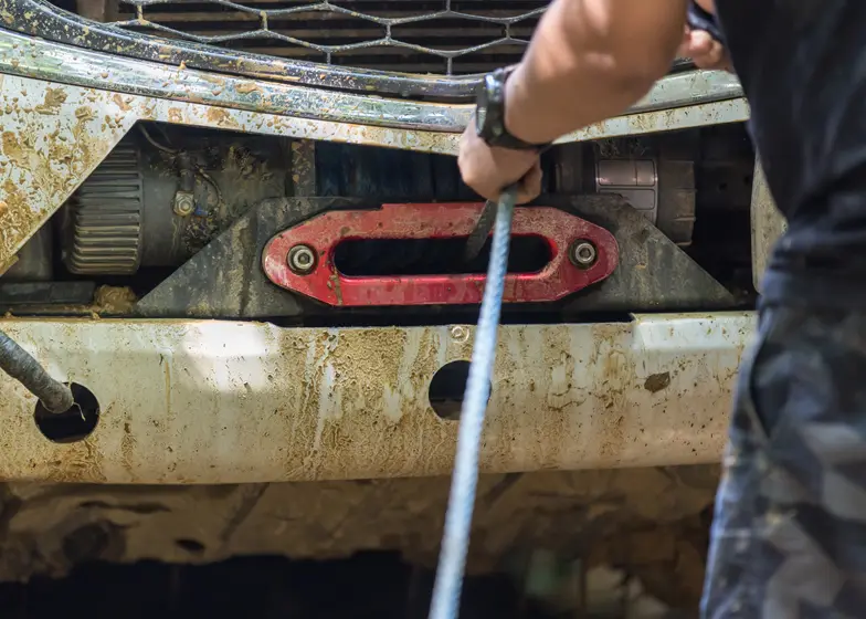 Close-up of a tow truck worker using a winch to remove a stuck vehicle, with a red recovery hook visible, during an unauthorized vehicle removal process.